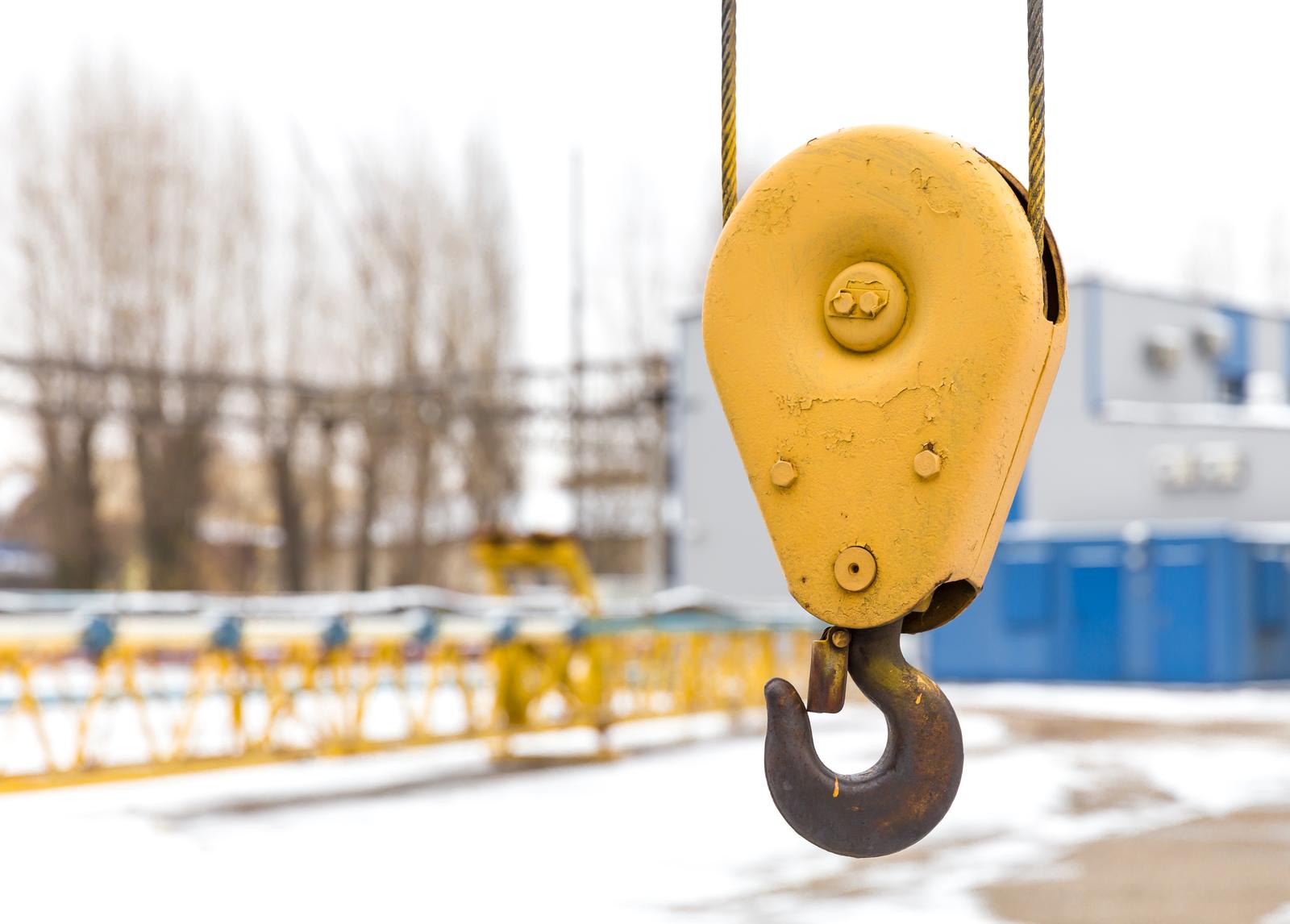 Yellow constraction crane hook with some industrial buildings on the background